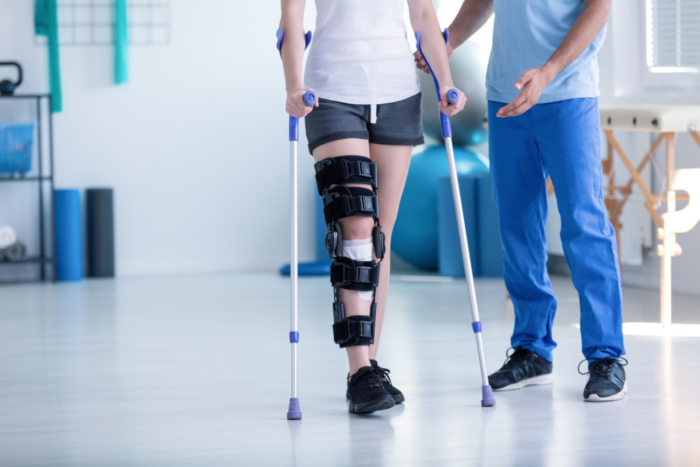 sportowiec u fizjoterapeuty który chodzi o kulach i z usztywniaczem na kolano